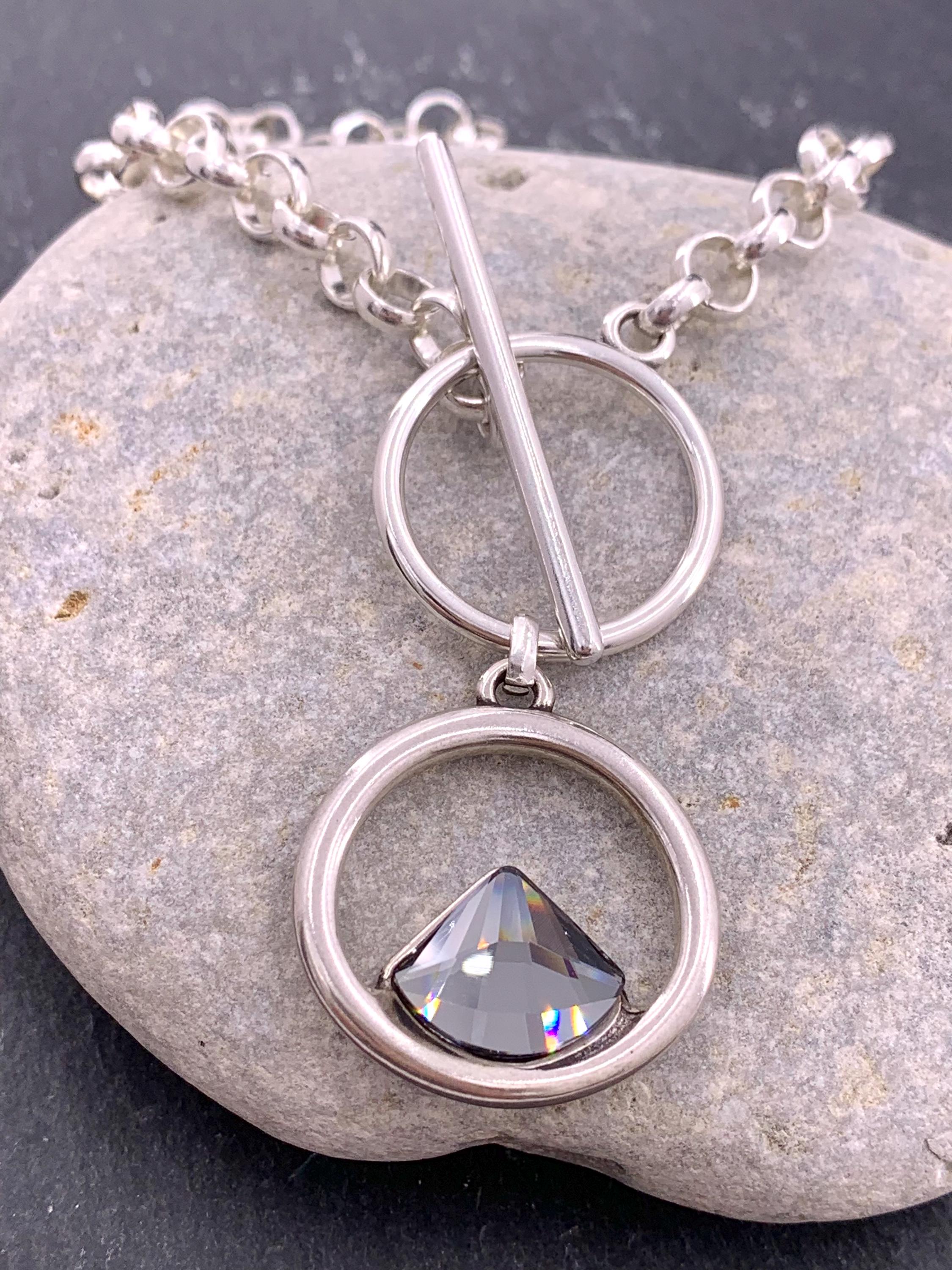 Elegant silver-plated necklace featuring a double-circle pendant with a brilliant triangular Swarovski crystal, finished with toggle clasp