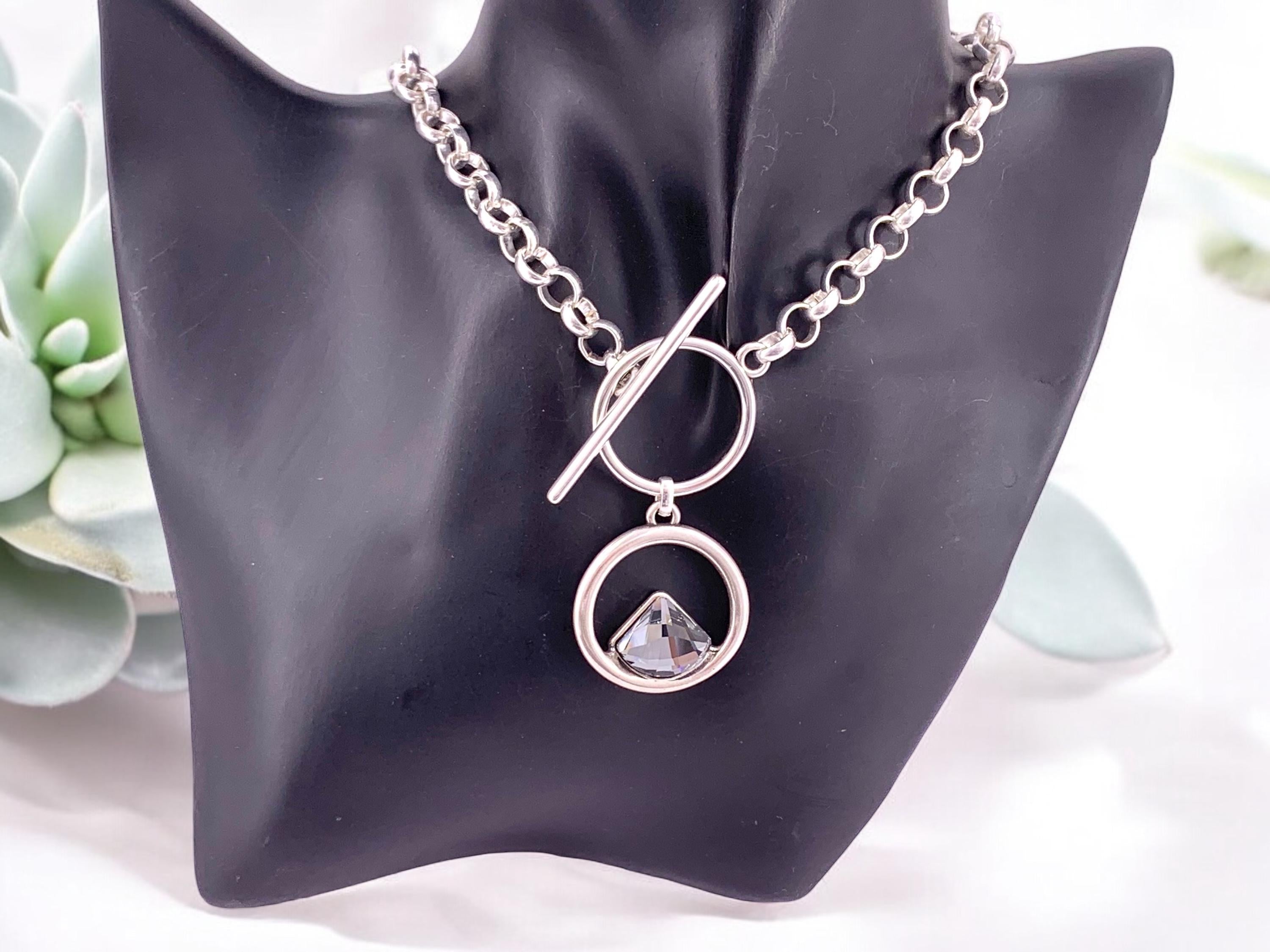 Elegant silver-plated necklace featuring a double-circle pendant with a brilliant triangular Swarovski crystal, finished with toggle clasp