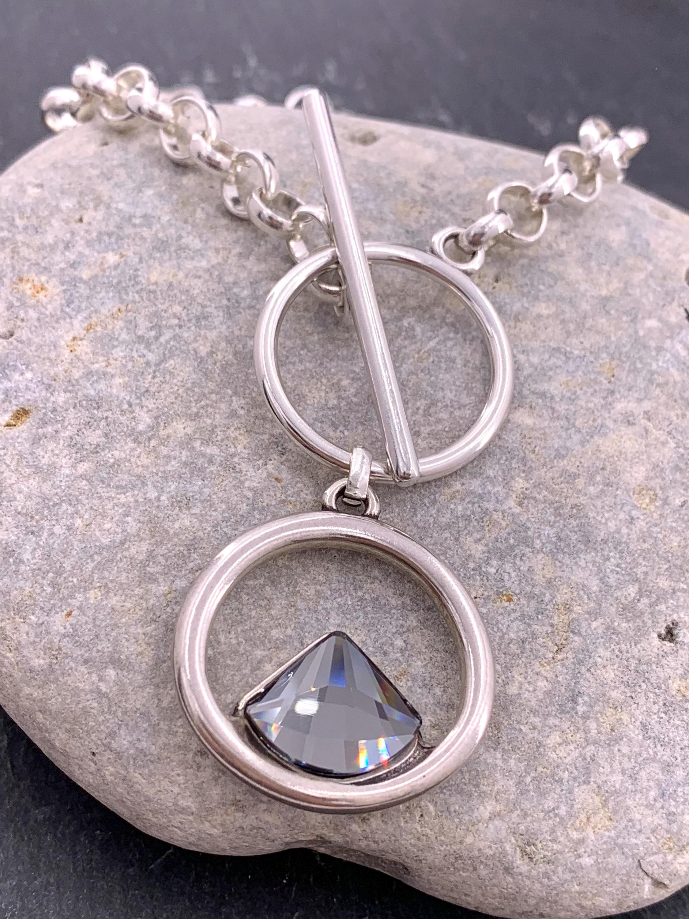 Elegant silver-plated necklace featuring a double-circle pendant with a brilliant triangular Swarovski crystal, finished with toggle clasp